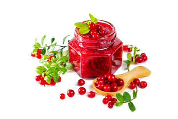 Jar of lingonberry jam with berries, leaves and wooden spoon isolated on white background.