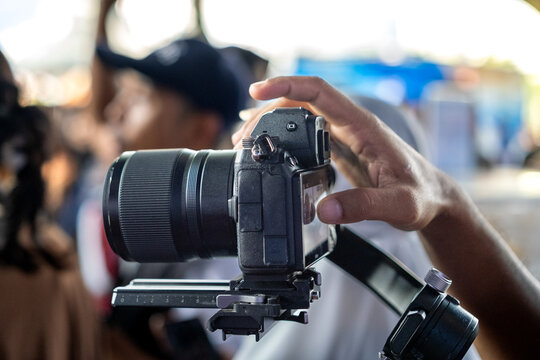 Close-up of a person operating a professional digital camera mounted on a stabilizer. Photographer adjusting settings for video or photo shooting in a busy environment.