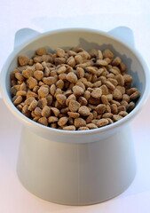 Dry cat food in a funny plastic bowl in the shape of a cat's head on a white background.