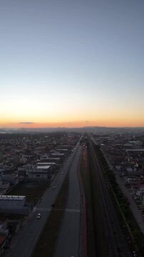 Vista a&eacute;rea de Mogi das Cruzes ao nascer do sol, com luz dourada iluminando pr&eacute;dios, montanhas ao fundo e a cidade ganhando vida
