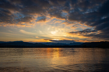 Naklejka premium Colourful cloudy sunset reflected in the ripples of a calm lake, with distant mountains, Lake Windermere, The Lake District, Cumbria, England
