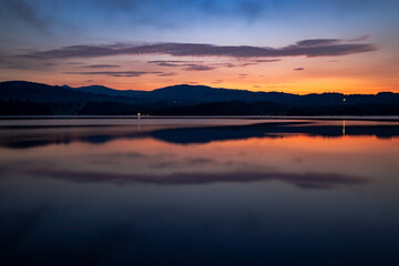 Pre-sunrise colours reflected in a lake and and clouds with distant hills, Lake Windermere, Cumbria, England 
