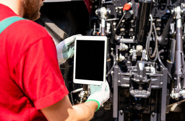 Agricultural mechanic using digital tablet for wireless machinery diagnostics. 