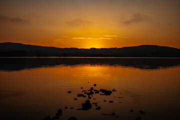 Pre-sunrise colours reflected in a lake and and clouds with distant hills, Lake Windermere, Cumbria, England 