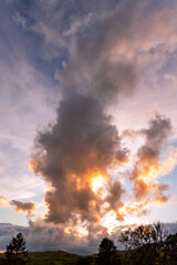 Billowing cloud lit by a setting sun above trees, hills and mountains, Latterbarrow, The Lake District, Cumbria, England,