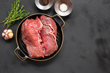 Raw beef meet with herbs and spices ready for cooking on black background, top view copy space for text