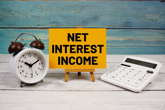 Net Interest Income (NII) text written on paper card with calculator and alarm clock on wooden background
