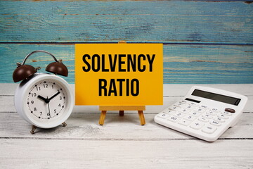 Solvency Ratio text written on paper card with calculator and alarm clock on wooden background