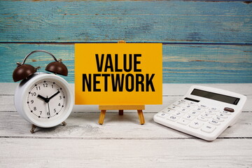 Value Network text written on paper card with calculator and alarm clock on wooden background