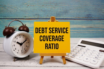 Debt Service Coverage Ratio (DSCR) text written on paper card with calculator and alarm clock on...