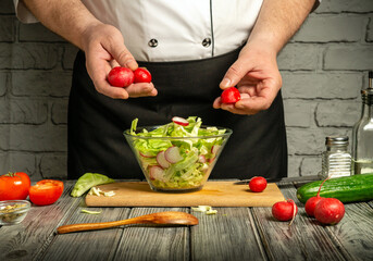 A chef skillfully mixes a fresh vegetable salad, holding radishes above a bowl of lettuce and other ingredients on a wooden countertop. The rustic kitchen adds charm to the setting