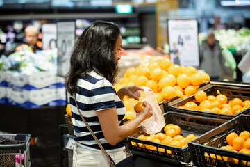 A middle-aged Filipina shopping for fresh mandarins in a supermarket, symbolizing healthy eating, real life, diversity, and everyday business.