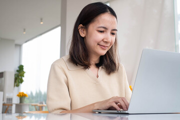 Asian woman working on laptop in cozy indoor space. Concept of freelance work, remote job, digital nomad lifestyle, online business, productivity, or modern technology for communication.