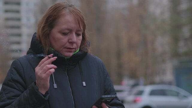 Woman enjoying a cigarette outside a building on a chilly day in a quiet urban atmosphere