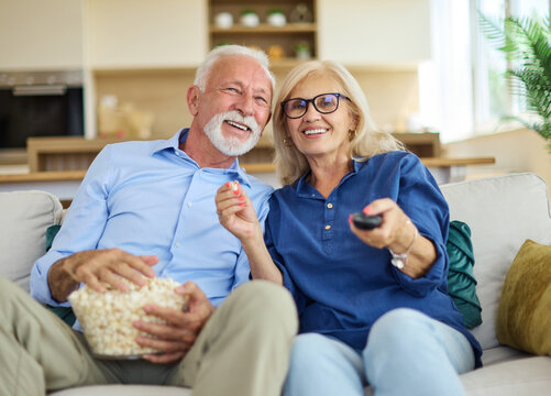 Portrait of an elderly senior happy couple watching tv together eating popcorn at home