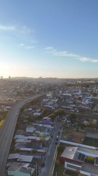 Vista a&eacute;rea de Mogi das Cruzes ao nascer do sol, com luz dourada iluminando pr&eacute;dios, montanhas ao fundo e a cidade ganhando vida.