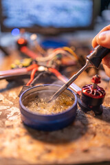 A close-up view of a person soldering electronic components on a workbench, showcasing a soldering iron and a motor part. neutral background, clear negative space, clean composition, balanced framing