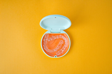 Clear Dental Aligners and Case on Orange Background. Orthodontic Mouthpieces.