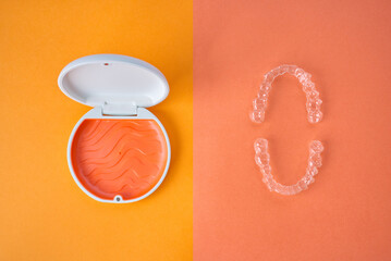 Clear Dental Aligners and Case on Orange and Pink Background. Orthodontic Mouthpieces.