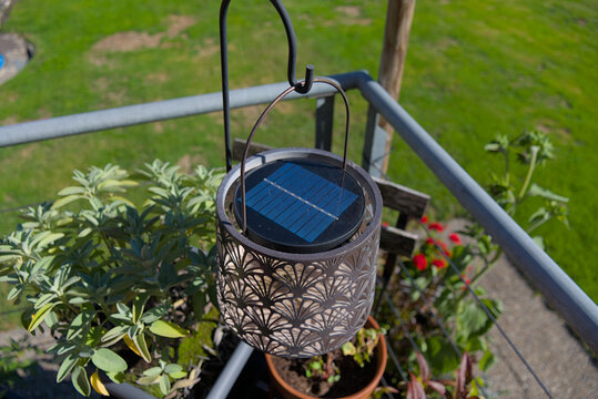 A decorative solar-powered lantern hangs on a balcony, its intricate pattern casting shadows in the sunlight. This image evokes an eco-friendly and stylish outdoor living theme, perfect for home decor