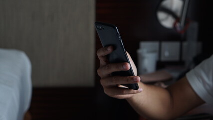Hand holding a smartphone beside bed