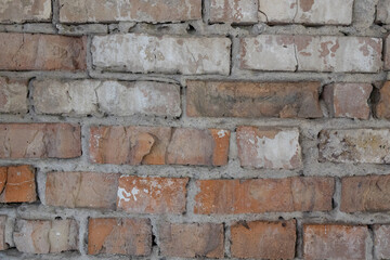 A close-up view of a textured brick wall showcasing various shades of red, orange, and gray bricks with visible mortar in between. The surface appears weathered and aged, highlighting the unique