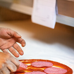 Hands preparing a pizza putting salami on pizza