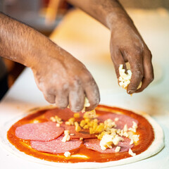 Hands preparing a pizza putting salami on pizza