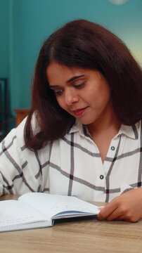 Indian woman at home writes notes in notebook then rereads lines showing careful focus and learning. Arabian girl at table studies written content reviewing details ensuring understanding and mastery.