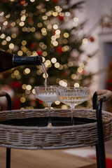 Champagne and glasses on a wicker tray in front of a decorated Christmas tree and fireplace