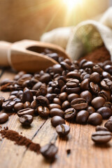 Fototapeta premium Close-up of roasted coffee beans scattered on a rustic wooden table with a wooden scoop and burlap sack in the background, warm sunlight creating a cozy and inviting atmosphere