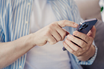 Man Wearing a Casual Striped Shirt Using a Modern Smartphone at Home in a Relaxed Indoor Setting
