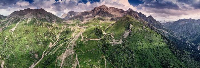 Breathtaking aerial view of winding roads ascending through vibrant green mountains, under a dramatic sky filled with clouds