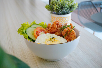 Indonesian rice bowl with fried chicken, boiled egg, fresh vegetables, and sambal sauce served in a modern white bowl