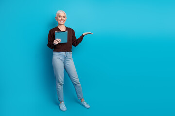 Smiling mature woman with tablet on blue background gesturing confidently and embracing happiness and leisure