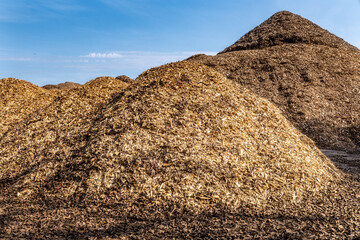 Large piles of wood chips and biomass for renewable energy and mulch production under blue sky in industrial storage area