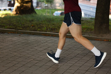 Athletic young man in sportswear running outdoors, closeup. Space for text