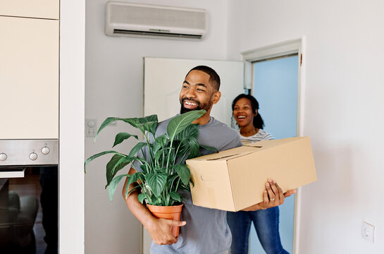 Young black couple moving into a new modern house, carrying boxes and arriving home together. Happy, excited and smiling husband and wife walking, entering and relocating after buying an apartment