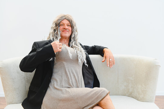 Senior man wearing wig and dress sitting on sofa