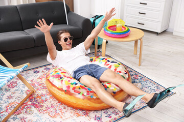 Happy man in sunglasses and flippers with inflatable ring having fun on floor at home. Dreaming about vacation at sea © New Africa