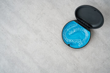 Clear dental aligner and blue case on marble table. Orthodontic mouthpiece storage.