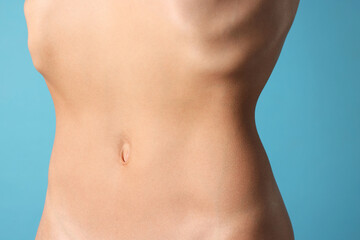 Woman with flat belly on light blue background, closeup