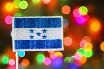 Embroidered Honduras flag in front of rainbow bokeh lights like fireworks, symbolizing New Year, national pride and Independence Day celebration.