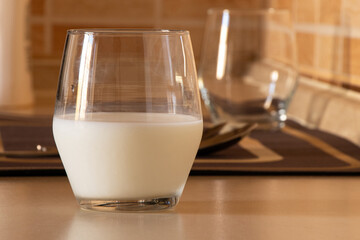 Transparent glass filled with milk which stands on the kitchen table