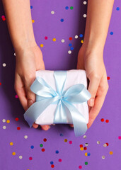 gift in female hands on a colored background with confetti top view.. Vertical photo format