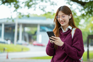  Asian female student in warm clothes using phone to chat with friends and ready for video call while in university.