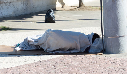 View of a homeless man sleeping on the ground next to an electric pole in the city of Salvador,...