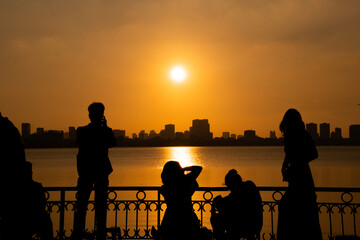 Obraz premium Golden sunset over the lake, silhouetted friends watching the glowing horizon in peaceful harmony.