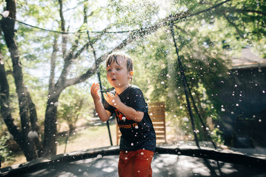 A young toddler jumps on the trampoline under a sprinkler in the summer in Oregon.