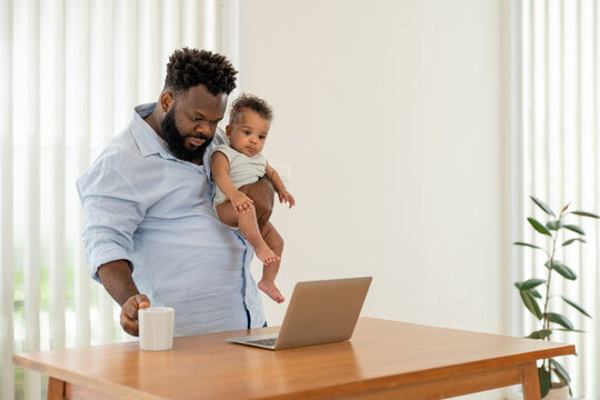 African father multitasking holding baby son, using laptop and drink coffee while work from home. Single dad parenting newborn boy at modern apartment - Powered by Adobe